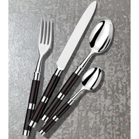 The Alain Saint-Joanis Carla Flatware Ebony 5 Piece Setting—hand-polished in France—features fork, knife, tablespoon, teaspoon, and salad fork with dark handles, arranged diagonally on a textured gray surface.