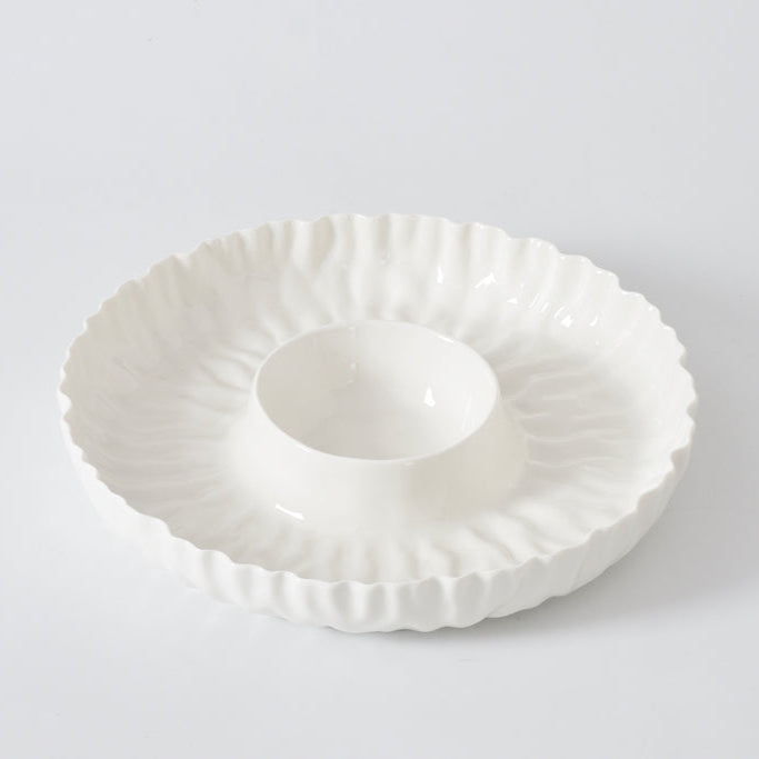 The PAMPA BAY Mascali Bianca Chip & Dip is a white porcelain serving dish with a textured wavy edge and raised round center. Microwave safe, it’s perfect for entertaining and looks stunning on any plain white background.
