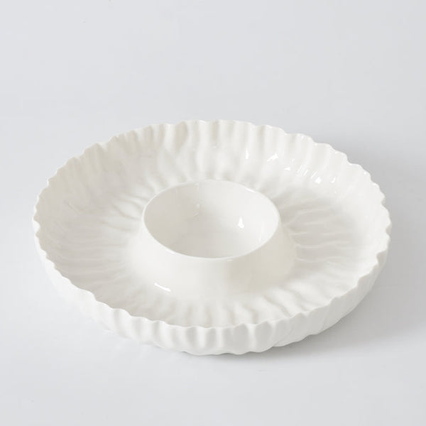 The PAMPA BAY Mascali Bianca Chip & Dip is a white porcelain serving dish with a textured wavy edge and raised round center. Microwave safe, it’s perfect for entertaining and looks stunning on any plain white background.