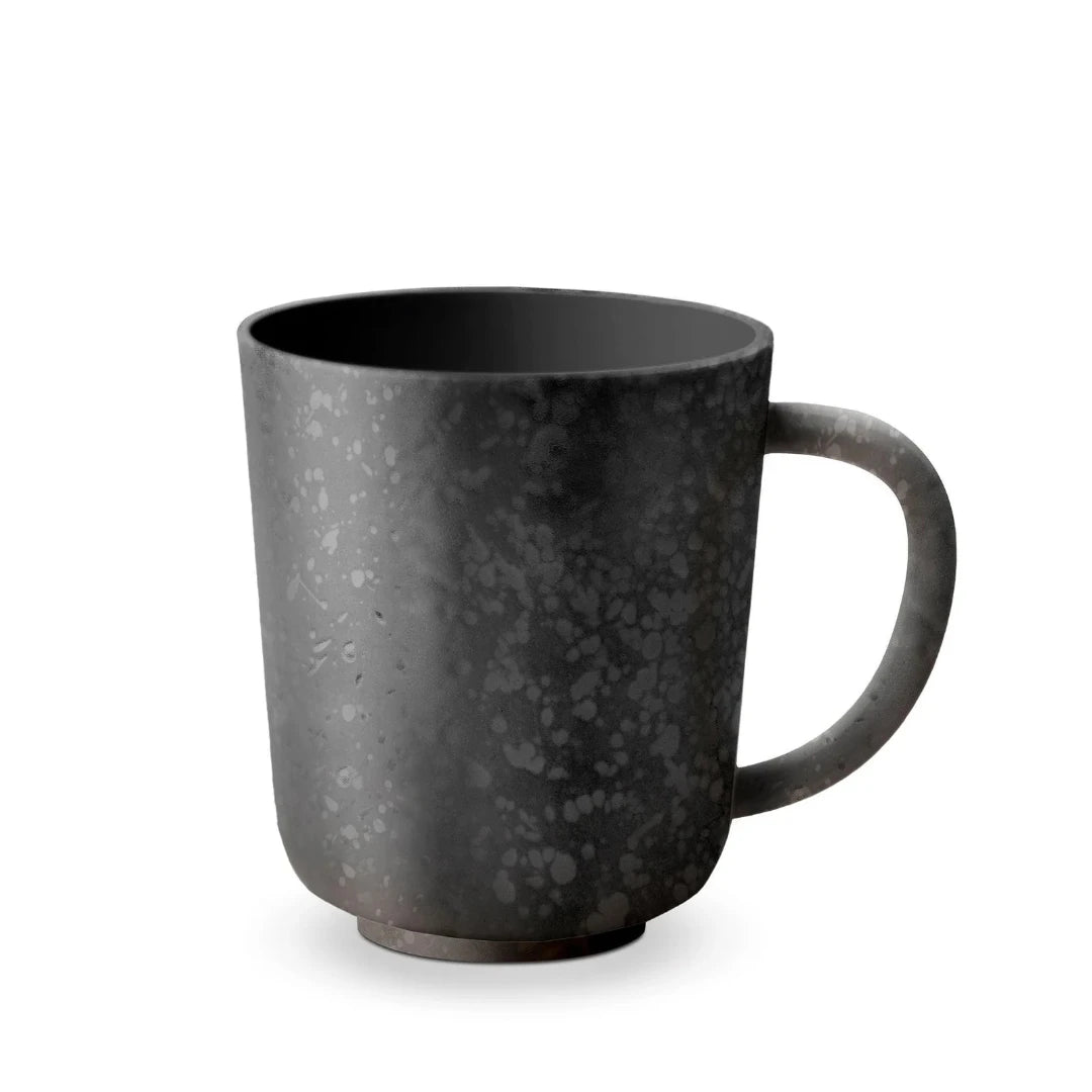 The Alchimie Dinnerware Black mug by L'Objet is a matte black ceramic piece with a handle and speckled pattern, featuring a sleek cylindrical shape—ideal for elevating your luxury tableware set.