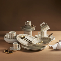 A beige and white patterned bone china set, the Amalfi Dinnerware Set 3 Piece Set by Greg Natale, featuring plates, bowls, and cups, is arranged on a brown surface with gold cutlery and dried lemon slices.