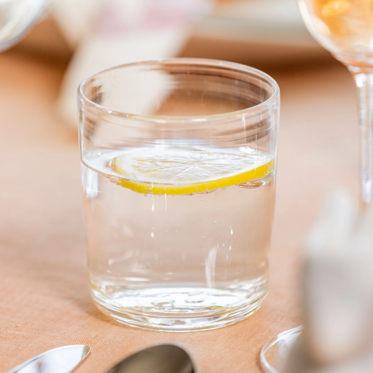 A hand-crafted glass from the Simon Pearce Walden Glassware Set/4, filled with water and topped with a lemon slice, sits on a textured surface.