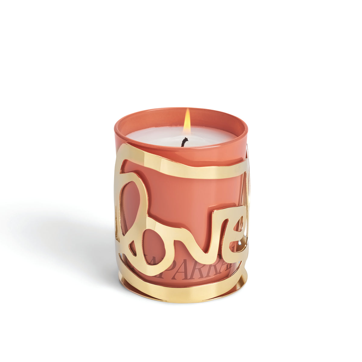 A lit pink luxury candle, the Love Candle - Chaparral by Amber Sakai, glows within a gold holder featuring a cutout design that spells “love.” The holder elegantly wraps around the candle, set against a plain white background. Inspired by Alexandra Grant’s signature style, this piece truly stands out as the perfect decorative accent.