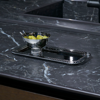 A silver bowl with green apples and a spoon sits on a silver tray, accented by the Anna New York Striations Silver Cocktail Picks Set/4 and Holder, atop a dark marble countertop with white veins.