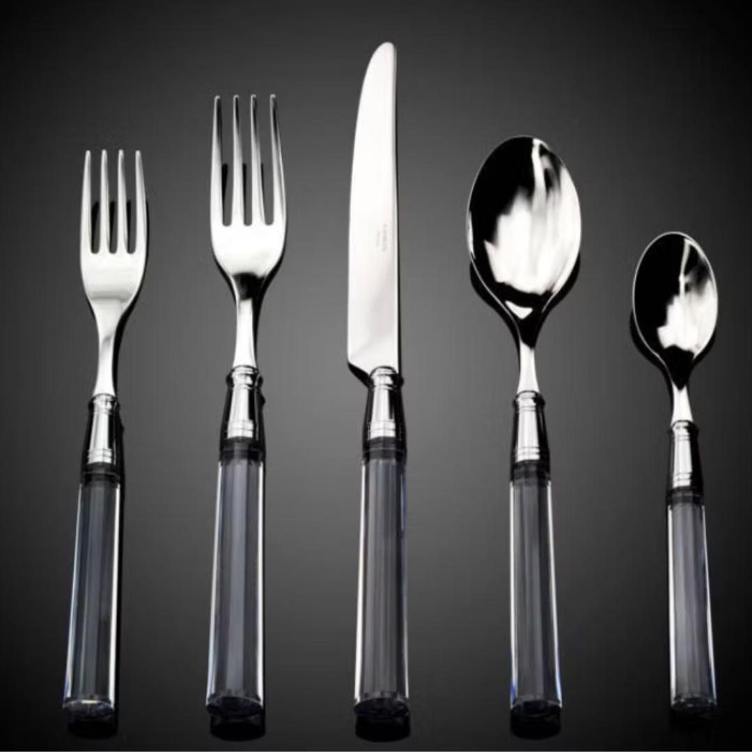 The Capdeco Doric Flatware 5 Piece Setting - Clear includes two forks, a knife, a spoon, and a soup spoon with stainless steel heads and clear handles, elegantly displayed upright against a dark background.