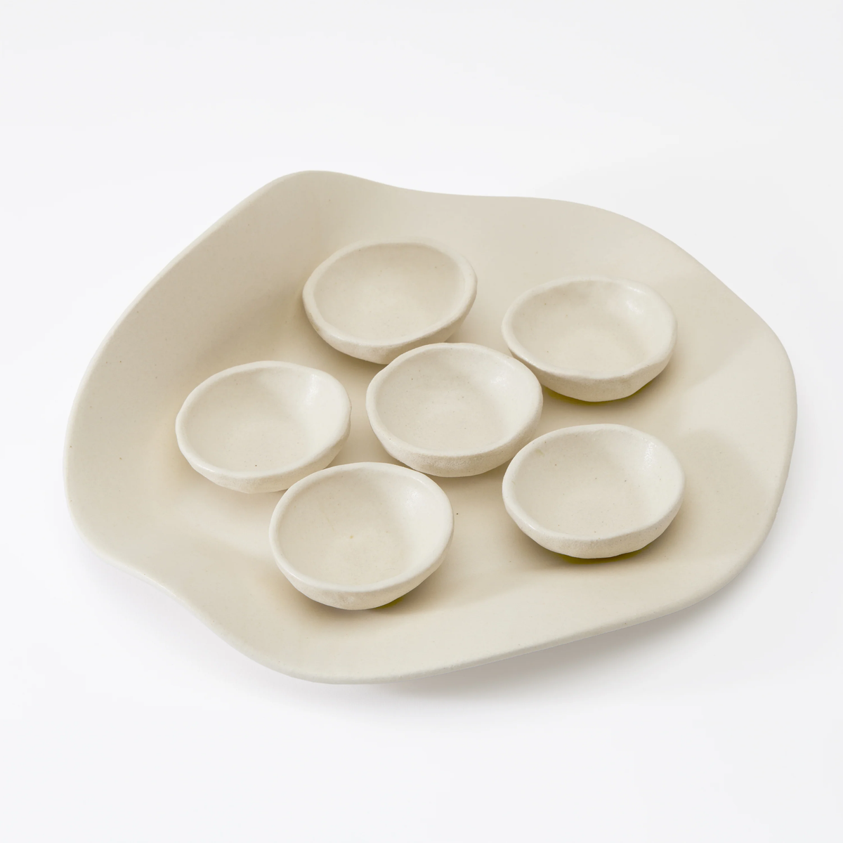 The Evie Seder Plate by Dumae features six small, round white bowls on an irregularly shaped handmade plate—ideal for an elegant Passover Seder or as stylish tableware.