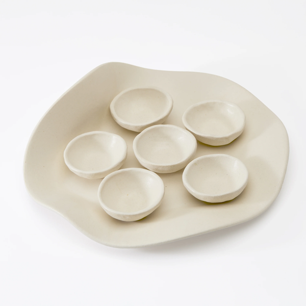 The Evie Seder Plate by Dumae features six small, round white bowls on an irregularly shaped handmade plate—ideal for an elegant Passover Seder or as stylish tableware.