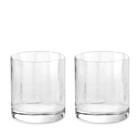 Two clear glass tumblers from the Iris Drinkware Collection by L'Objet, featuring thick bases and a hand-cut design, are placed side by side on a white background.