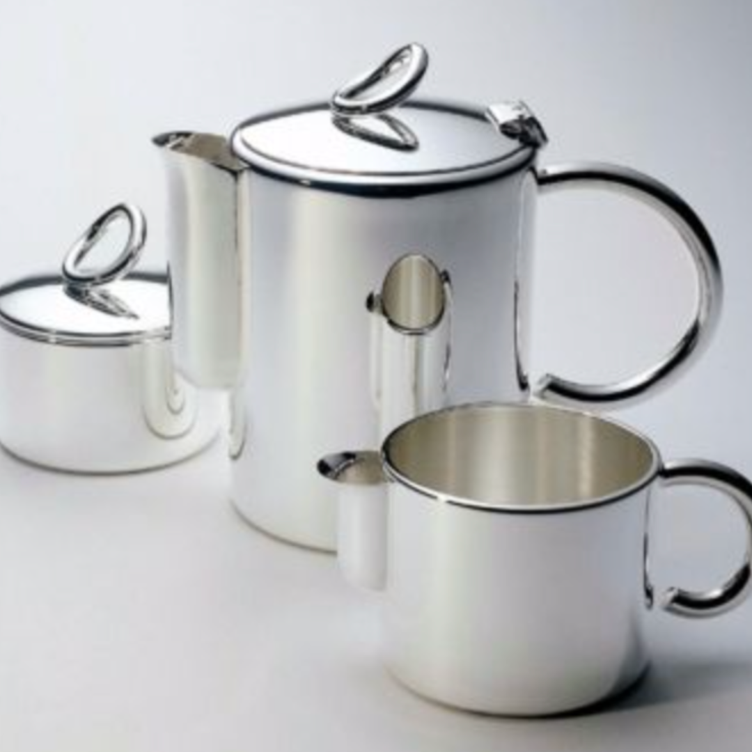 The Vertigo Silver Plated Creamer by Christofle is a luxury accessory with smooth, reflective surfaces and rounded handles, shown alongside a silver teapot and modern pitcher against a light background.