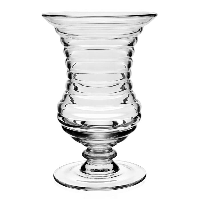 The Ripples Footed Vase by William Yeoward features clear glass with a wide, flared rim, ribbed rounded body, and short pedestal base. Symmetrical ridges create a ripple effect, ideal for elegant flower arrangements.
