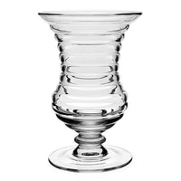 The Ripples Footed Vase by William Yeoward features clear glass with a wide, flared rim, ribbed rounded body, and short pedestal base. Symmetrical ridges create a ripple effect, ideal for elegant flower arrangements.