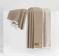 A tan and cream Aspen Reversible Throw by Lands Downunder, featuring white trim, is draped over a white surface. A brown label reading "Aspen Throw" is attached to one cozy corner of the soft blanket.