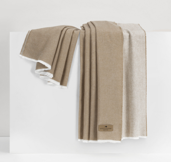 A tan and cream Aspen Reversible Throw by Lands Downunder, featuring white trim, is draped over a white surface. A brown label reading "Aspen Throw" is attached to one cozy corner of the soft blanket.