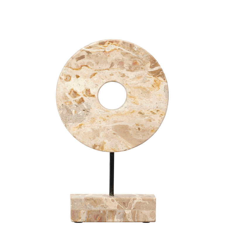 The Jamie Young Marble Cream Circle Disk on Stand features a round, cream marble sculpture with a central hole, set on a black metal stand and rectangular stone base—an elegant, celestial-inspired decor piece.
