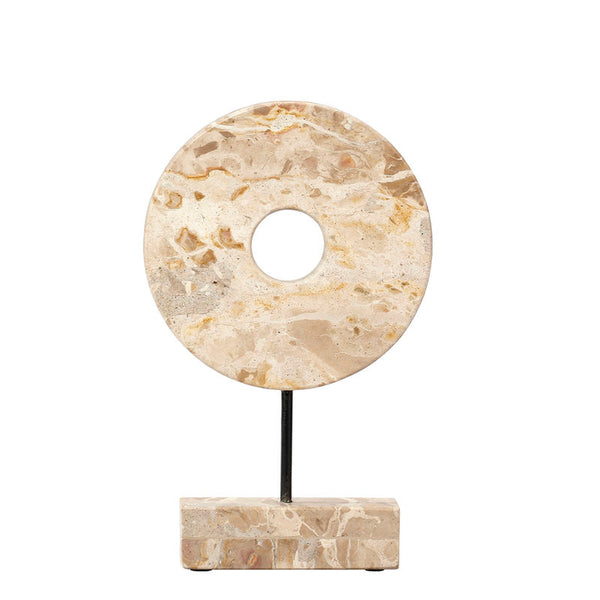 The Jamie Young Marble Cream Circle Disk on Stand features a round, cream marble sculpture with a central hole, set on a black metal stand and rectangular stone base—an elegant, celestial-inspired decor piece.