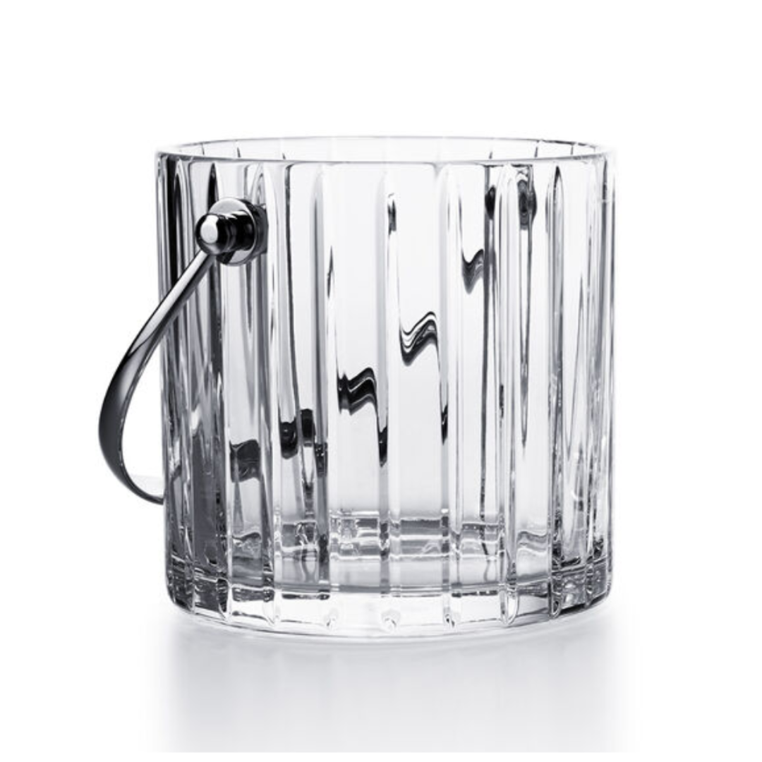 The Baccarat Harmonie Ice Bucket features vertical ridges and a metal handle, crafted from clear crystal—luxury barware inspired by timeless elegance.