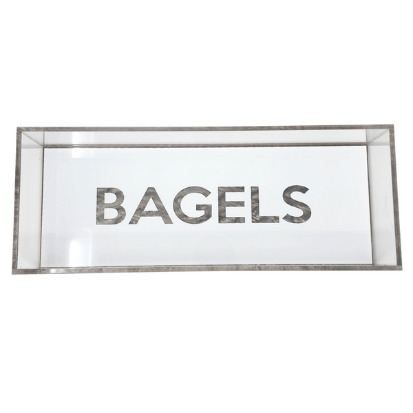 The Eye Candy Bagel Tray is a rectangular glass display case with "BAGELS" in bold letters on the front, a food-safe acrylic tray for bagels, and stylish silver marble acrylic accents.