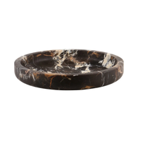 The Flat Honed Marble Bowl by Designs by Marble Crafter is a round, shallow bowl crafted from dark marble featuring striking white and brown veining. Photographed against a plain white background, this statement piece effortlessly enhances any space with its modern elegance.