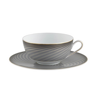 The Oskar Dinnerware teacup and saucer by Raynaud feature a gray and gold geometric design with thin horizontal lines and a gold rim on fine white Limoges porcelain.