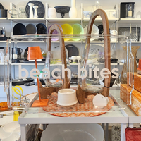 A glass display case labeled "Beach Bites" showcases the Eye Candy Deluxe Acrylic Beach Bites Tray alongside decorative containers and dishes in a shop stocked with eclectic kitchenware, ceramics, and outdoor entertaining plates, bowls, and vases.