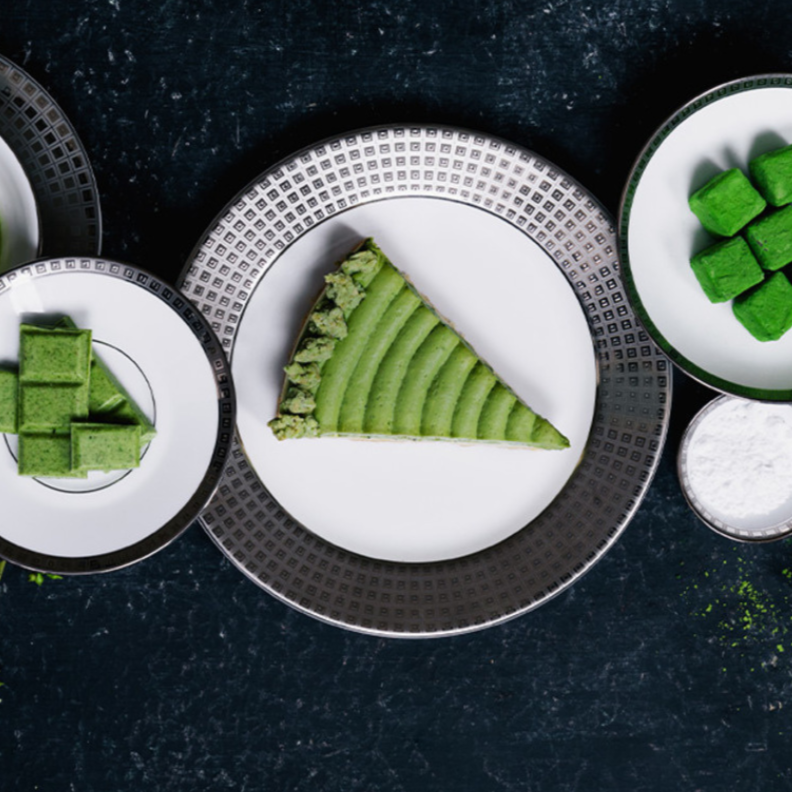 A slice of green matcha cake on a Bernardaud Athena Platinum Dinnerware plate, surrounded by matching Bernardaud pieces holding matcha treats and powdered sugar, all artfully arranged on a dark surface.