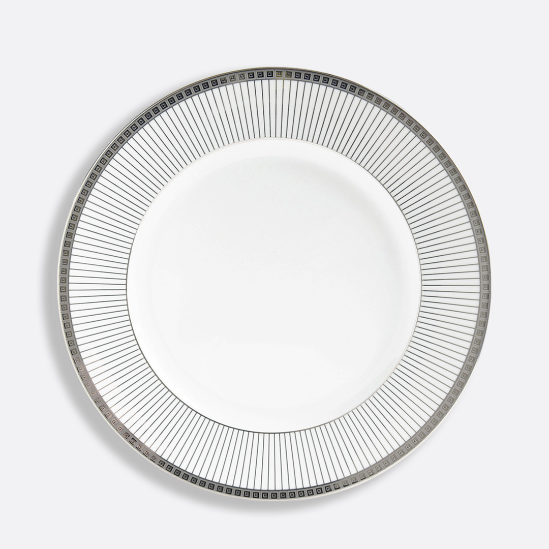 The Bernardaud Athena Platinum Dinnerware features a white porcelain plate with a platinum border of radiating thin lines and small squares along the rim, set against a plain light gray background, highlighting its elegant design.