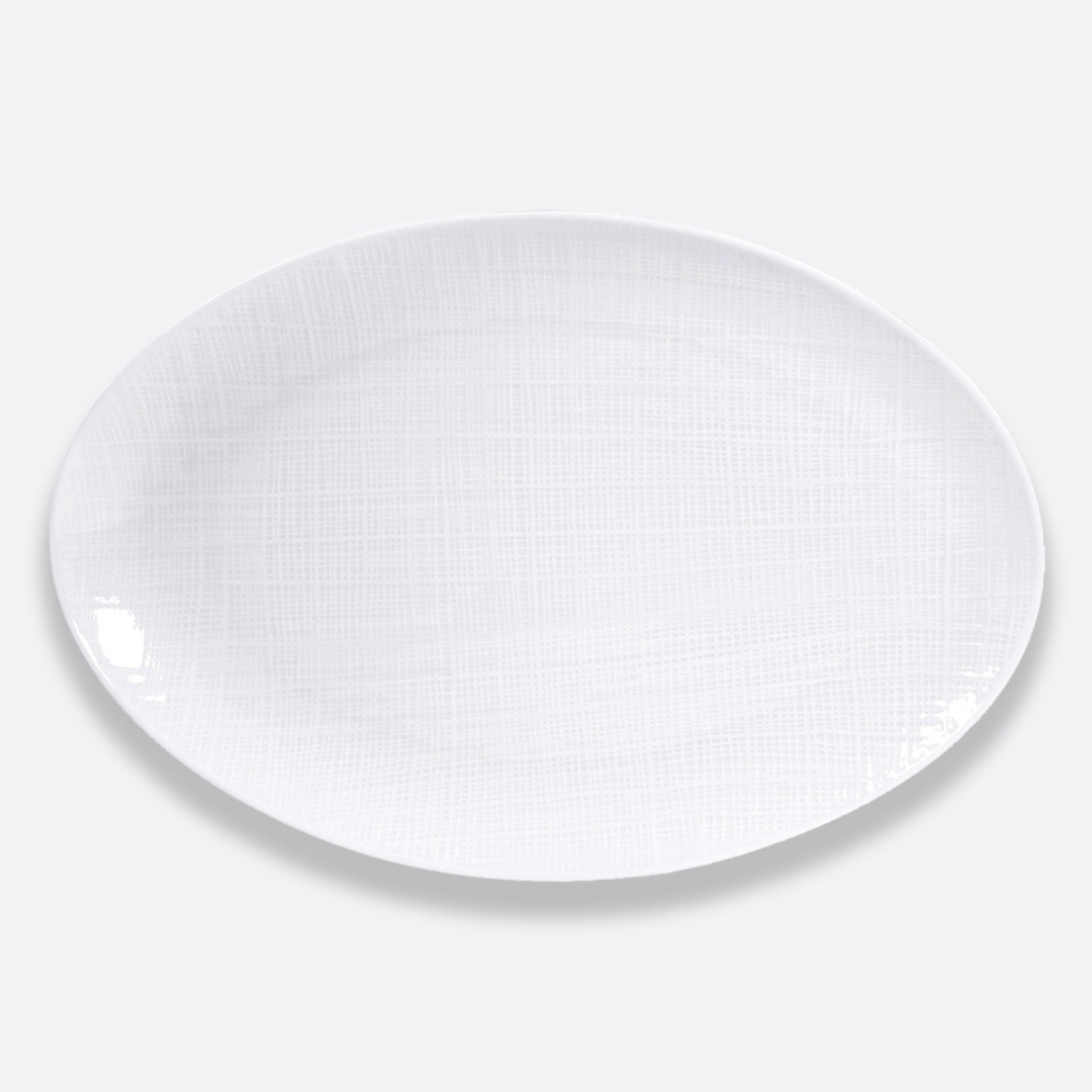 A white, oval plate from Bernardaud’s Organza White Dinnerware collection, featuring a subtle texture in Limoges porcelain, is displayed against a plain light gray background.