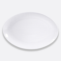 A white, oval plate from Bernardaud’s Organza White Dinnerware collection, featuring a subtle texture in Limoges porcelain, is displayed against a plain light gray background.