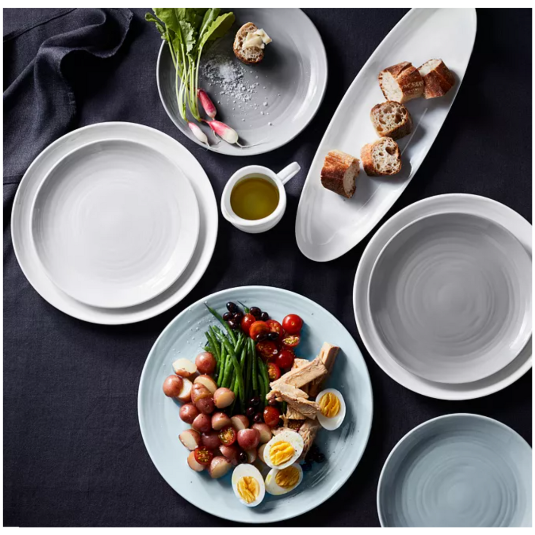 A table set with Bernardaud Origine Dinnerware White—Limoges porcelain plates featuring vegetables, eggs, tuna, radishes, and ginger—plus sliced bread and a small cup of olive oil on a dark tablecloth.