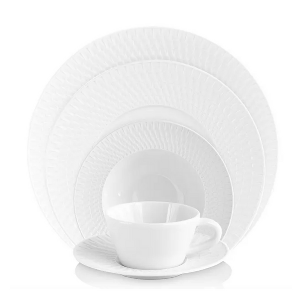 The Bernardaud Twist White Dinnerware set, featuring geometric-patterned plates, soup bowl, bread plate, and teacup with saucer, is elegantly arranged against a white background for a refined dining display.