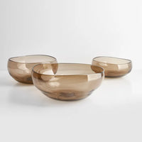 The Nesting Glass Bowl Collection Wheat by Gary Bodker features three translucent brown handblown bowls in varying sizes, each with smooth, rounded shapes and slightly irregular rims, perfect as salad bowls or serving dishes.