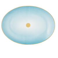 The Aura Dinnerware by Raynaud features a flat, oval plate with concentric turquoise lines radiating from a golden center, fading to white near the middle. A gold-trimmed rim completes its contemporary look.