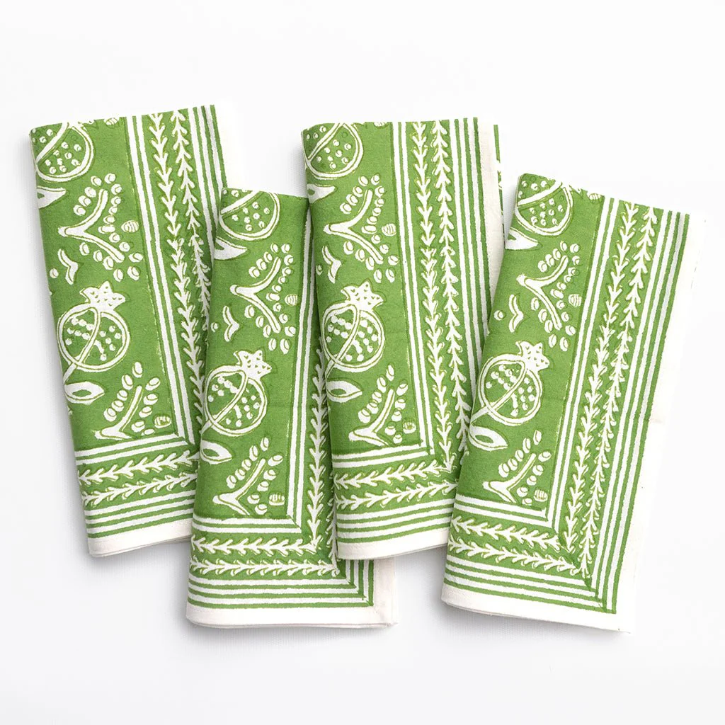 The Pomegranate Napkin Set of 4 by Pomegranate features green cotton napkins with white botanical and fruit patterns, including pomegranates, neatly folded and arranged side by side on a white background.