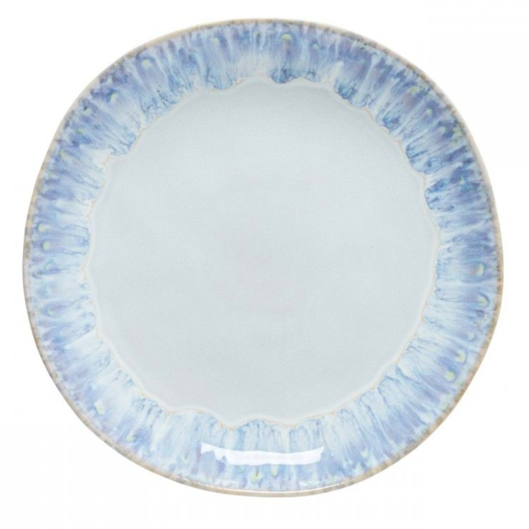 The Costa Nova Brisa Blue Dinnerware features a round ceramic plate with a pale blue center and blue-purple patterned rim, viewed from above. Crafted in Portugal from quality stoneware.