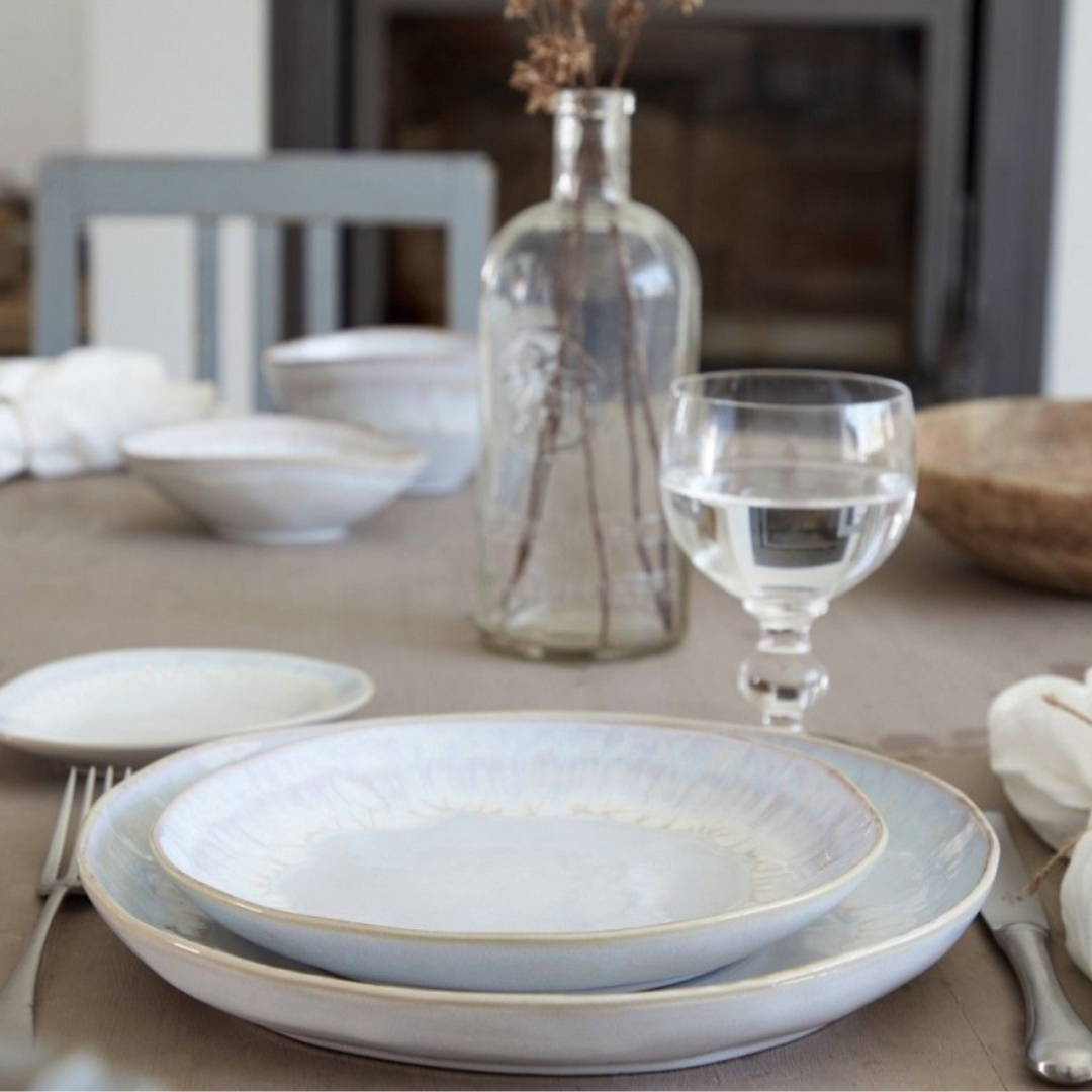 Elegant table setting with Casafina/Costa Nova Brisa Sal Dinnerware made in Portugal, a glass of water, cutlery, white napkin, and clear bottle with dried flowers. Soft natural light enhances the tranquil ambiance.