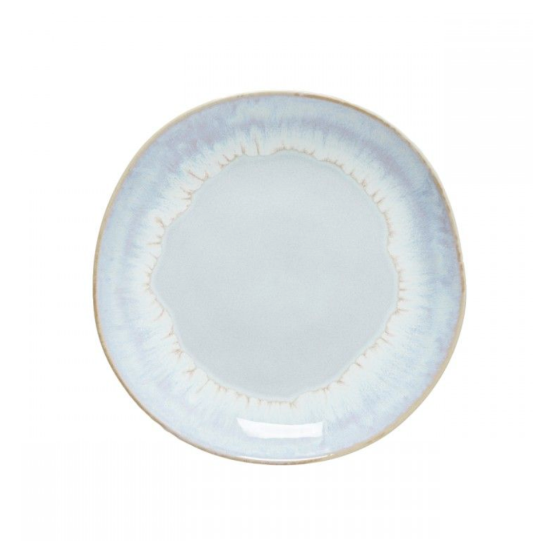 The Brisa Sal Dinnerware by Casafina/Costa Nova is a round ceramic plate inspired by the Algarve coast, featuring a white center, subtle uneven light blue glaze, thin beige rim, and a slightly irregular edge.