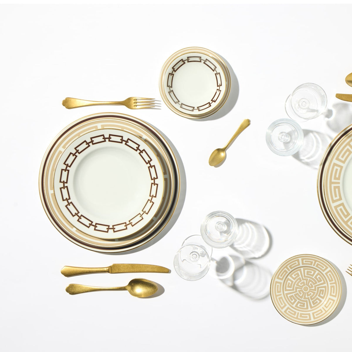 A flat lay of Ginori 1735’s Catene Ebony Brown Dinnerware with gold accents and a porcelain bowl, styled with gold cutlery on a white background.