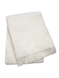 The Basic Waffle Throw by A Soft Idea, in cream with fringed edges, is crafted from a soft cotton-acrylic blend and shown folded on a white background.