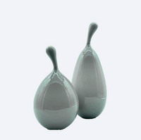 Two glossy, pear-shaped Volume Vessel Dove Grey sculptures by Tyler Barry Design, each with an elongated stem—one slightly taller—form a striking sculptural accent, positioned close together against a plain light background.