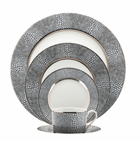 The Makassar Gray & Platinum Dinnerware set by Royal Limoges/Bia Cordon Bleu includes a handmade dinner plate, salad plate, bread plate, dessert plate, and cup with saucer in a black and white pebble design with metallic rims.