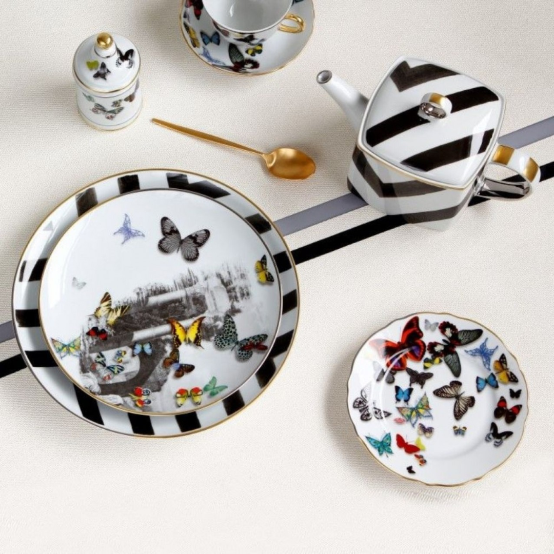 The Butterfly Parade Dinnerware by Vista Alegre features black and white stripes with colorful butterfly designs, including a teapot, plates, cup, jar, and gold spoon—ideal for mix-and-match dinnerware enthusiasts.