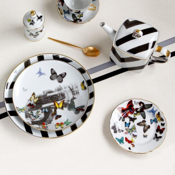 The Butterfly Parade Dinnerware by Vista Alegre features black and white stripes with colorful butterfly designs, including a teapot, plates, cup, jar, and gold spoon—ideal for mix-and-match dinnerware enthusiasts.