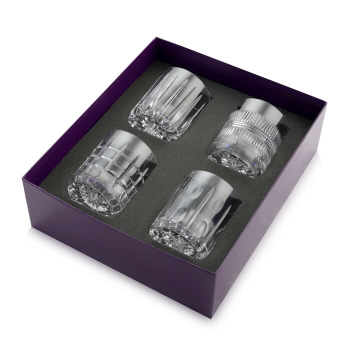 The William Yeoward Skye Drinkware Set of 4 features crystal whiskey glasses with unique cut patterns, beautifully arranged in a black foam insert within a purple gift box.