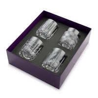 The William Yeoward Skye Drinkware Set of 4 features crystal whiskey glasses with unique cut patterns, beautifully arranged in a black foam insert within a purple gift box.