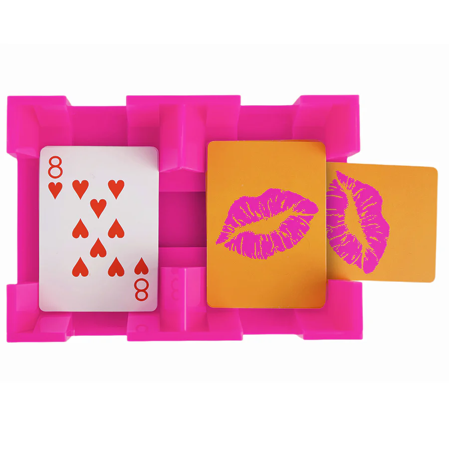 The Canasta Spinner by Canasta Sets is a unique pink card holder featuring three cards—one eight of hearts, two with lipstick kiss prints—perfect for adding flair to your canasta game night on an orange background.