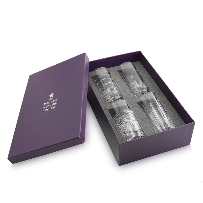 A purple box with William Yeoward on the lid, open to show four clear, intricately designed Skye Drinkware glasses securely nestled in black foam.