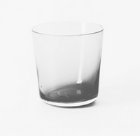 The Gary Bodker Everyday Glass Clear, a transparent tumbler ideal for daily use, rests on a white surface with gentle shadows and a minimalist backdrop.