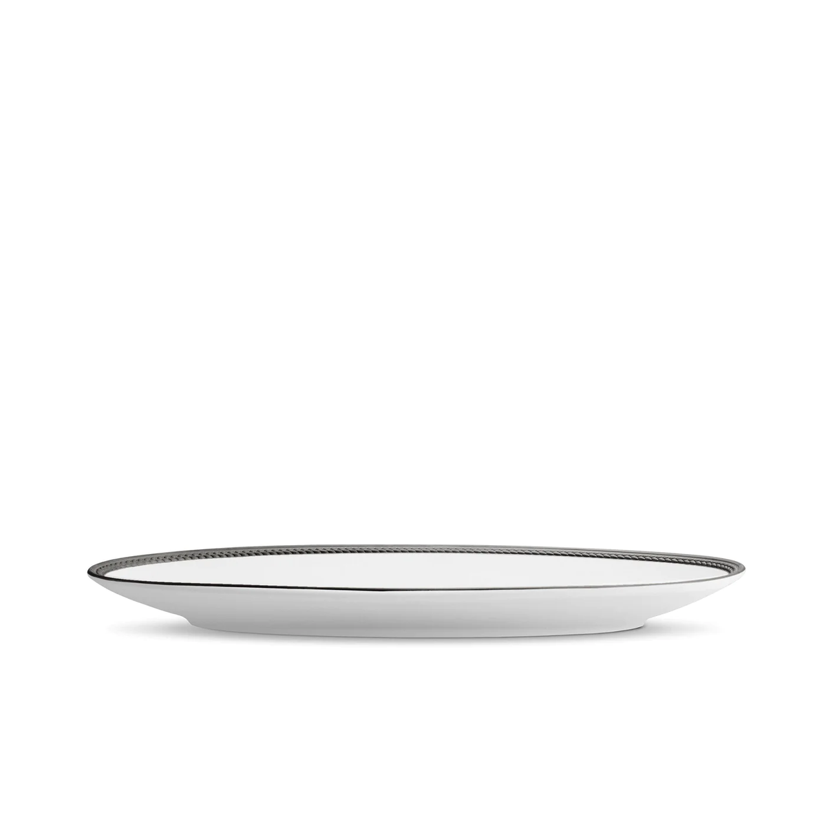 The Soie Tressée Black Dinnerware by L'Objet features a white ceramic plate with a thin, dark rim, displayed from the side on a white background, capturing the refined elegance of luxury porcelain.