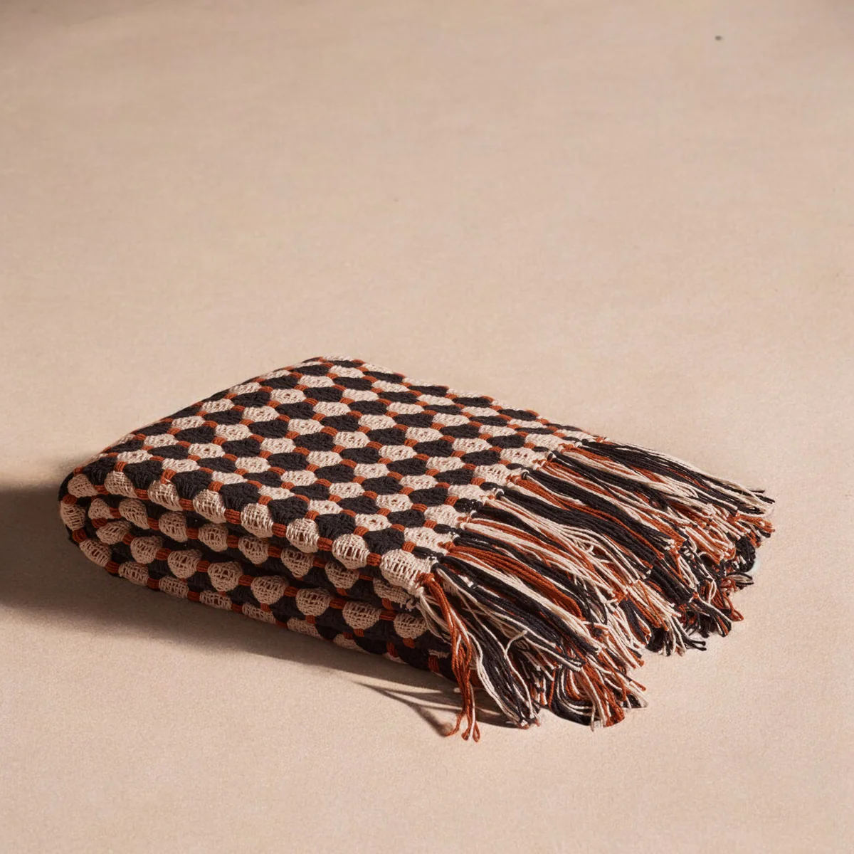 The Hampton Cotton Throw by Meso Goods is a folded cotton blanket with black, white, and rust-colored geometric circles. Crafted in a handloom flatweave, it has a wool fringe on one side.