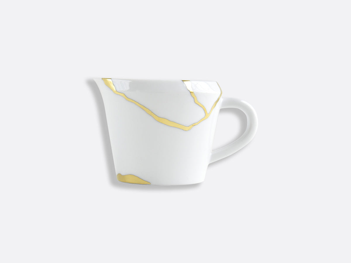 The Bernardaud Kintsugi Dinnerware white ceramic mug features gold-colored, irregular crack-like lines inspired by the Kintsugi art, highlighted against a plain light gray background and finished with a sleek handle.